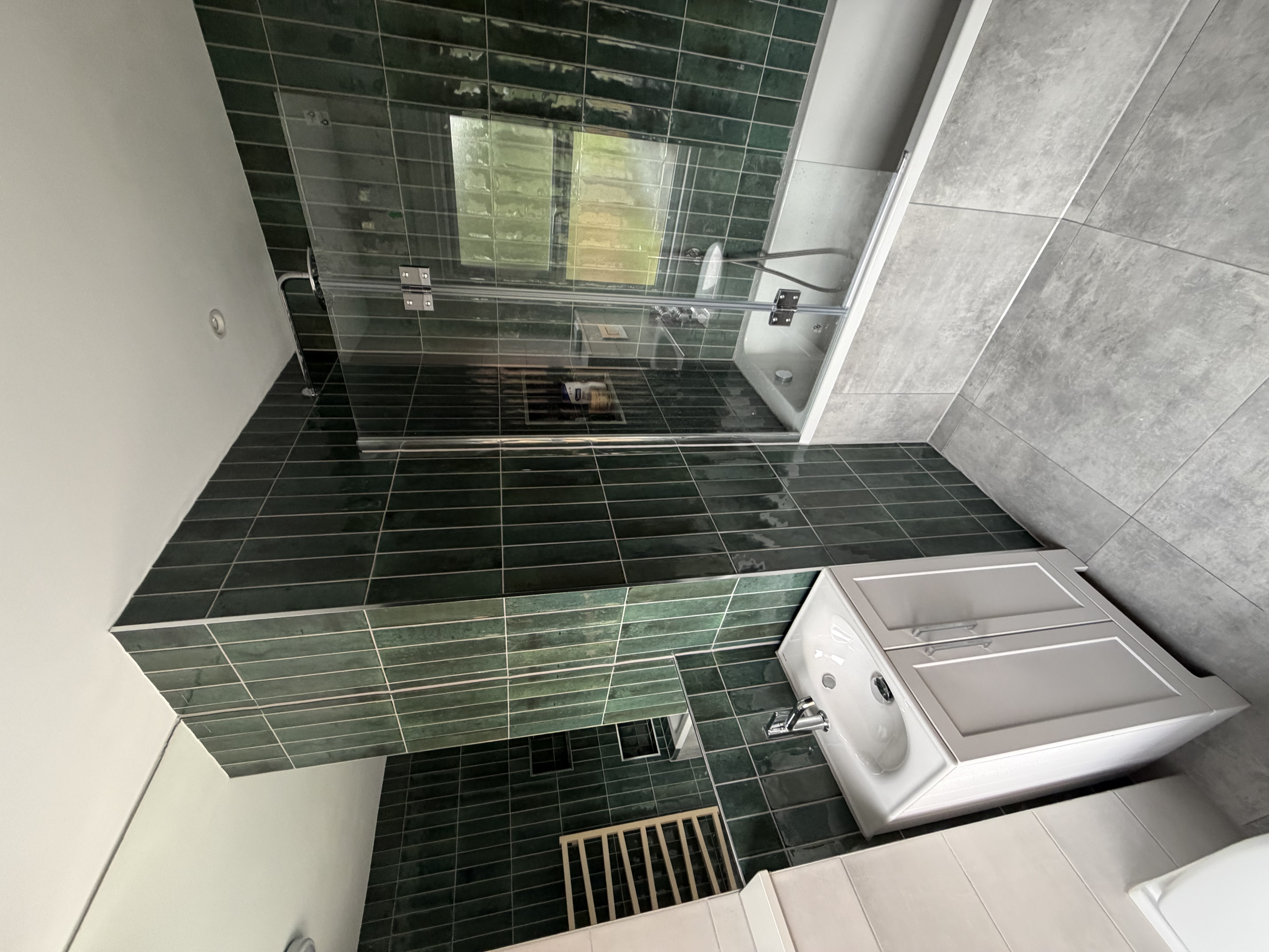 Bathroom with green wall tiles, a white vanity basin and a bath with a glass shower screen